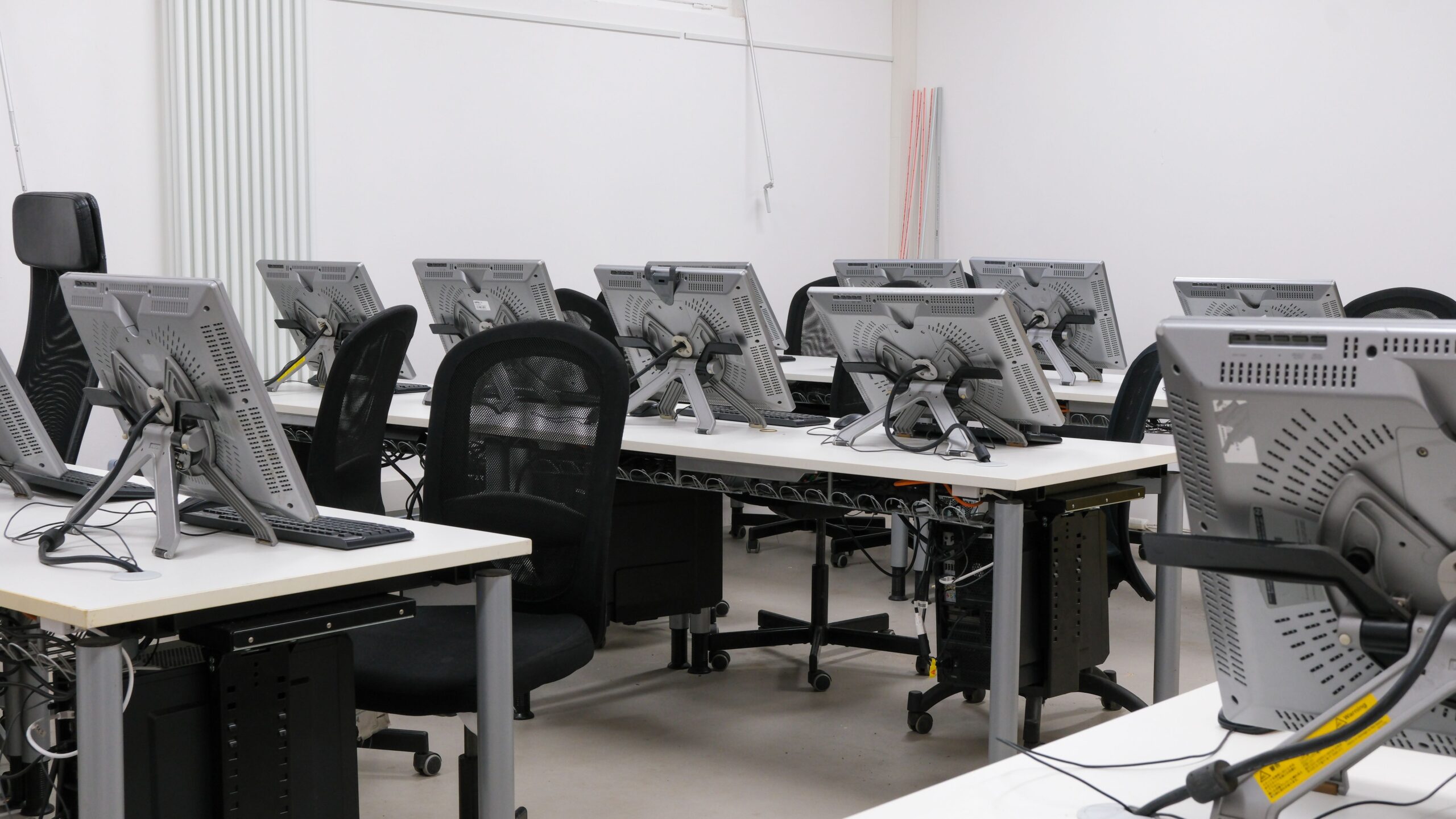 An empty computer lab featuring multiple workstations with monitors and chairs, ready for use.